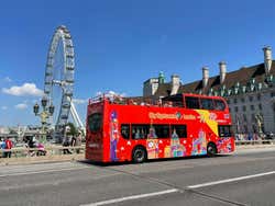 A red tourist bus drives past the London Eye