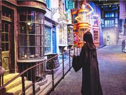 A girl in a black robe holds a wand looking down Diagon Alley